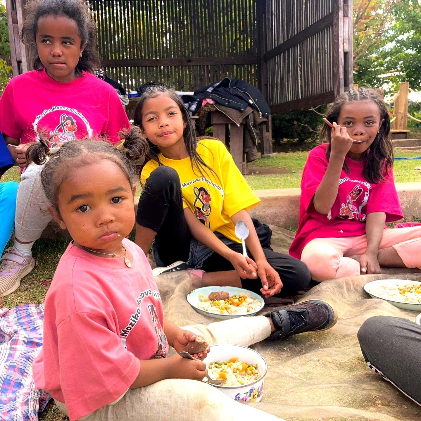 Children sitting on the ground outside eating a meal